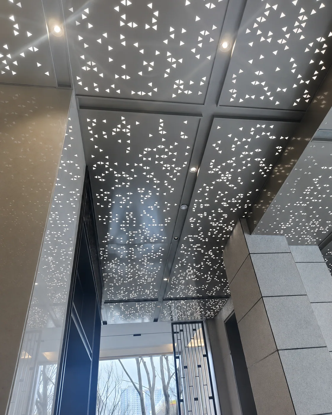 Perforated metal ceiling panels with triangular openings in a commercial lobby