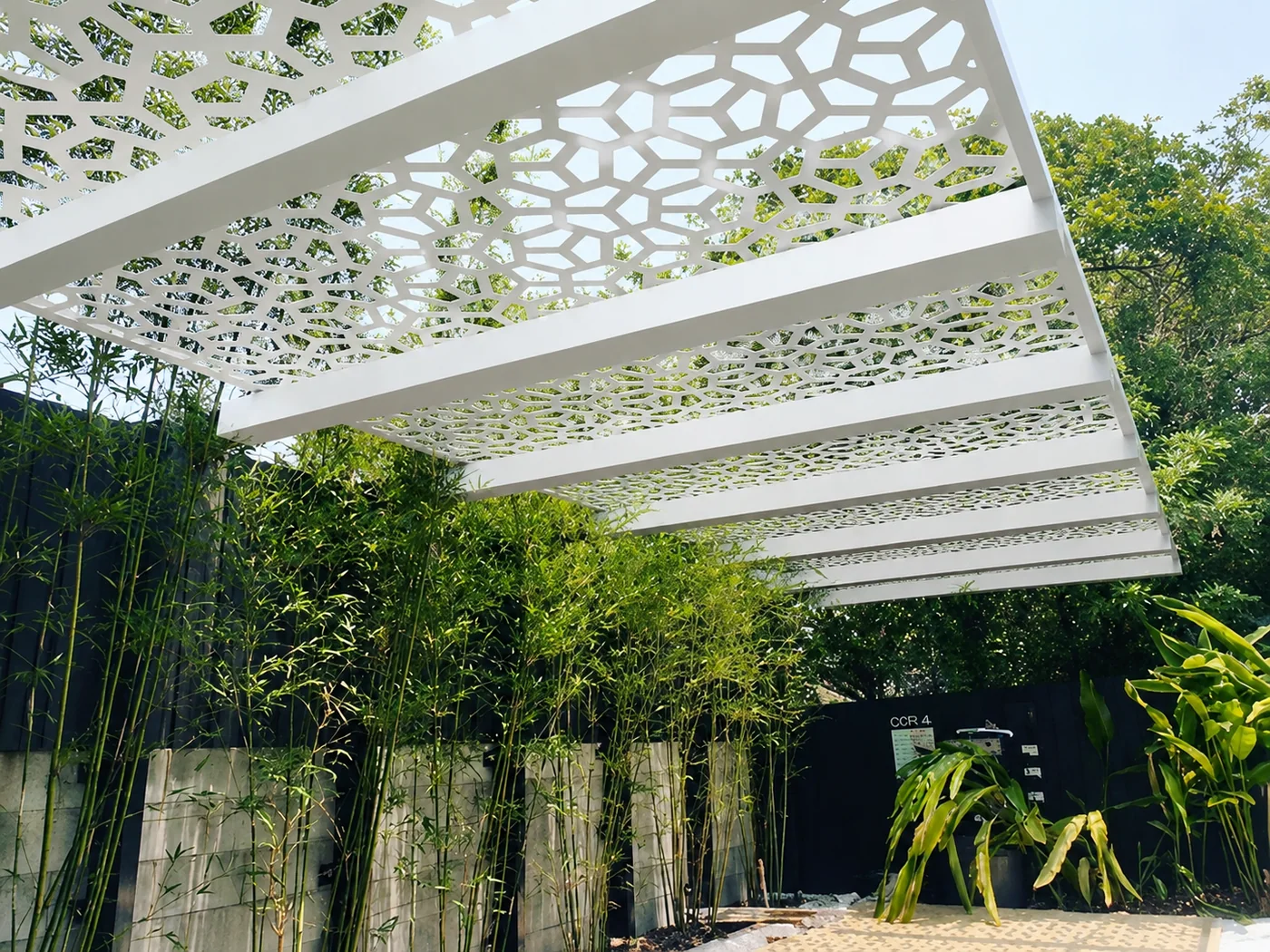 White perforated metal ceiling sunshade panels in an outdoor landscaped space