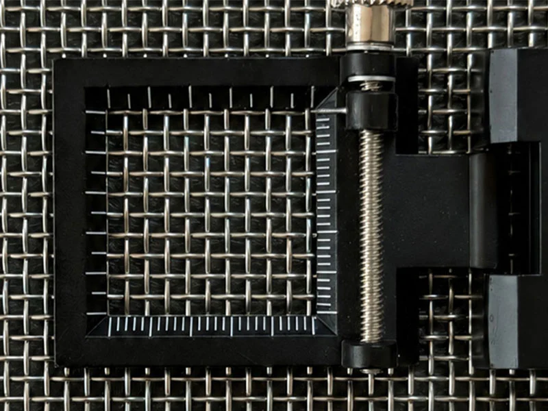 Close-up of square-opening stainless steel plain weave wire mesh under a folding inspection magnifier
